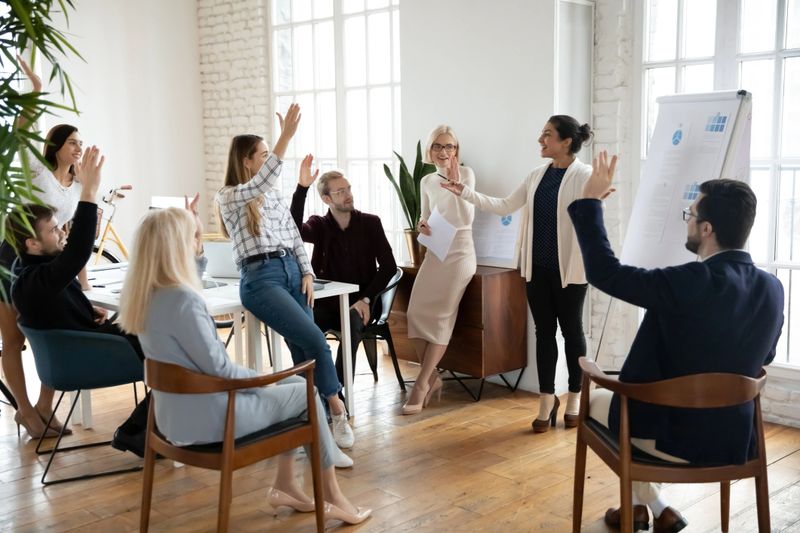 Motivated employees raising hands, asking coach at training. Presenter finishing workshop with questions from engaged audience. Indian female business leader interacting with team at corporate meeting