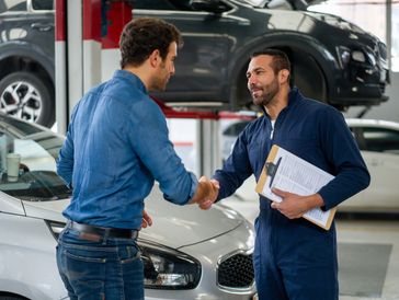 A mechanic and customer shake hands in an auto repair shop.