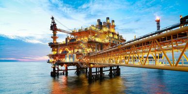 Illuminated offshore oil rig at sunset over calm sea.