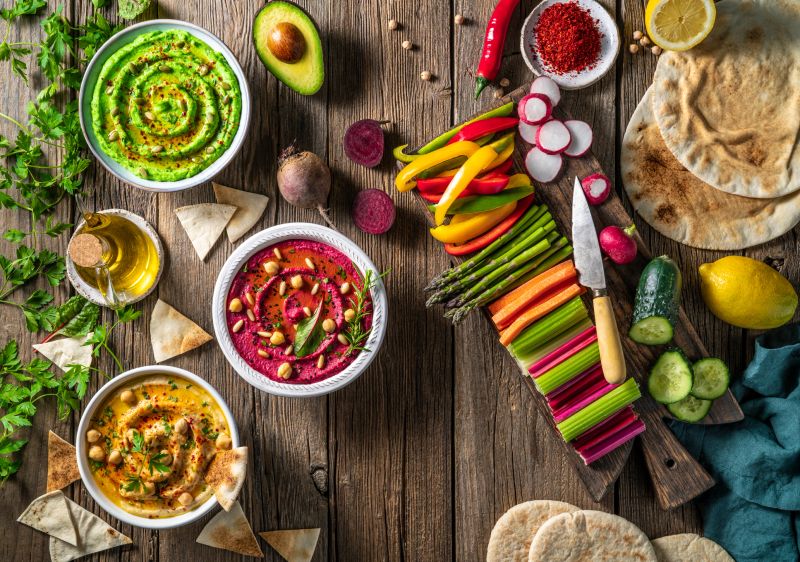 Hummus Three bowl of chickpeas, avocado and beetroot with cut vegetables for dip on rustic wooden table board background