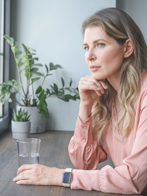 Woman in pink blouse looking thoughtfully out the window.