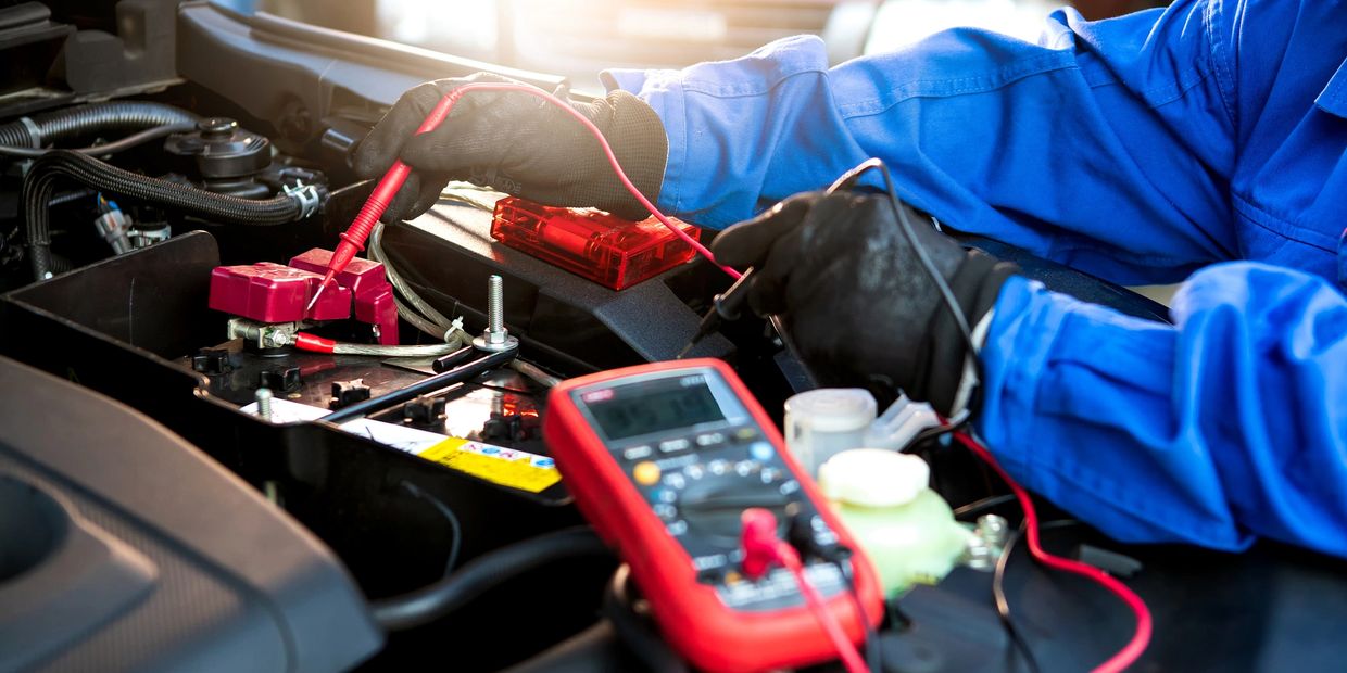 Technician testing a car battery with a multimeter under the hood.