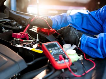 Mechanic testing a car battery with a multimeter under the hood.