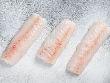 Three raw fish fillets on a textured surface.