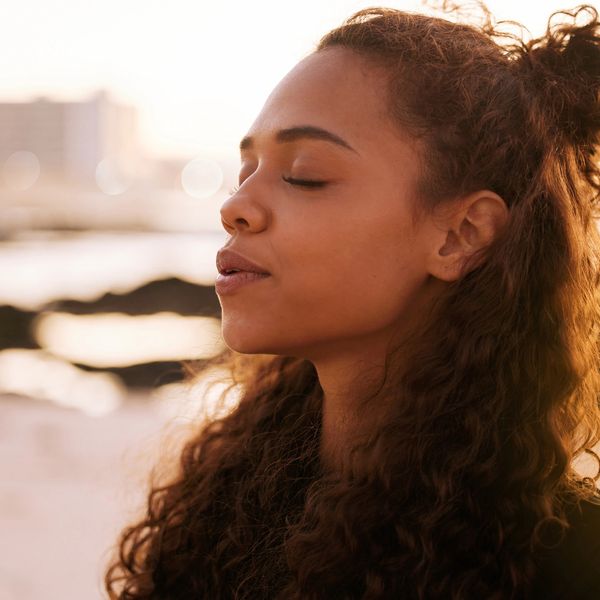 Woman with closed eyes in peaceful outdoor setting.