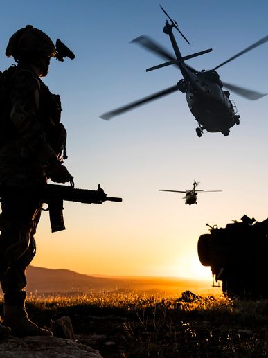 Silhouette of soldier with helicopters at sunset.