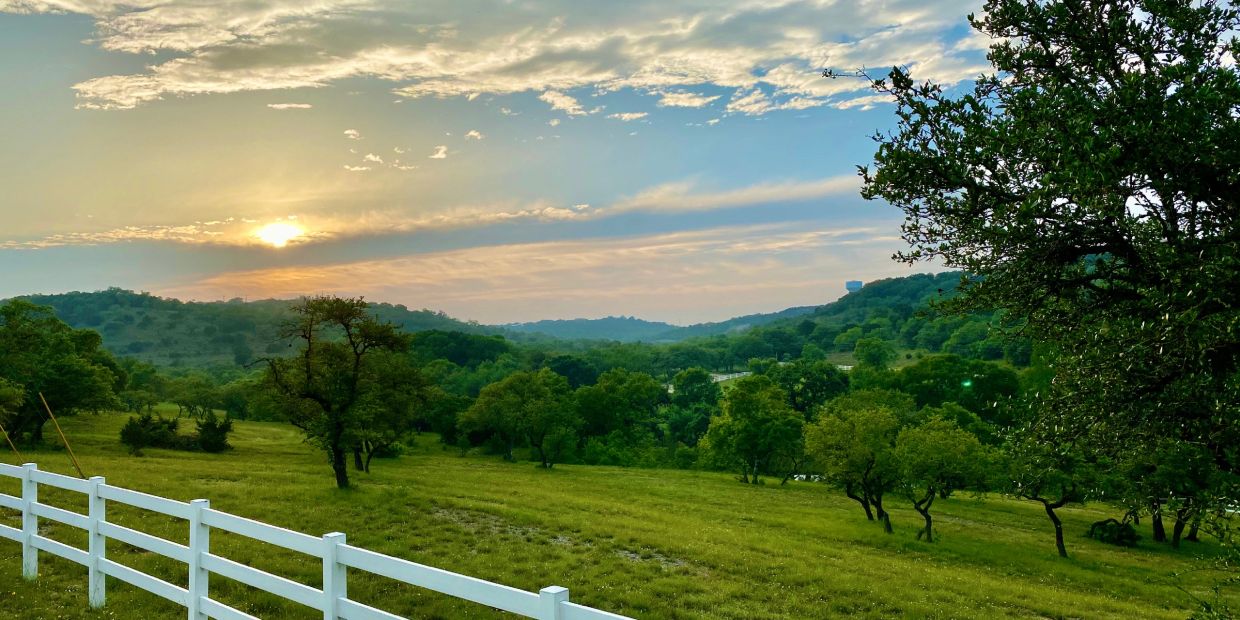 Sunset over rolling green hills with a white fence.