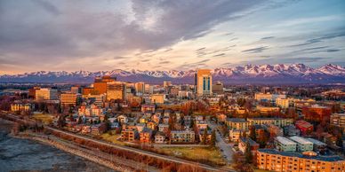 Cityscape of Anchorage at sunset with snowy mountains in the background.