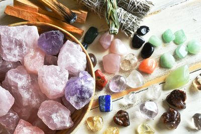 Various colorful healing crystals and sage bundles arranged on a wooden surface.