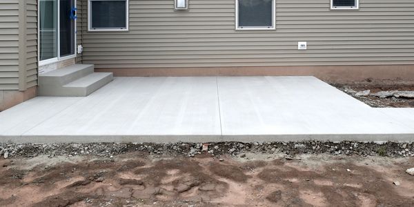 Freshly poured concrete patio at the back of a house with steps leading to a sliding door.