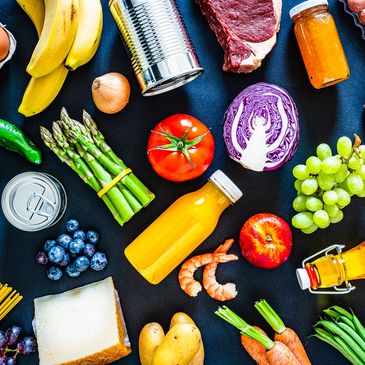 Assortment of fresh fruits, vegetables, and groceries on a dark background.