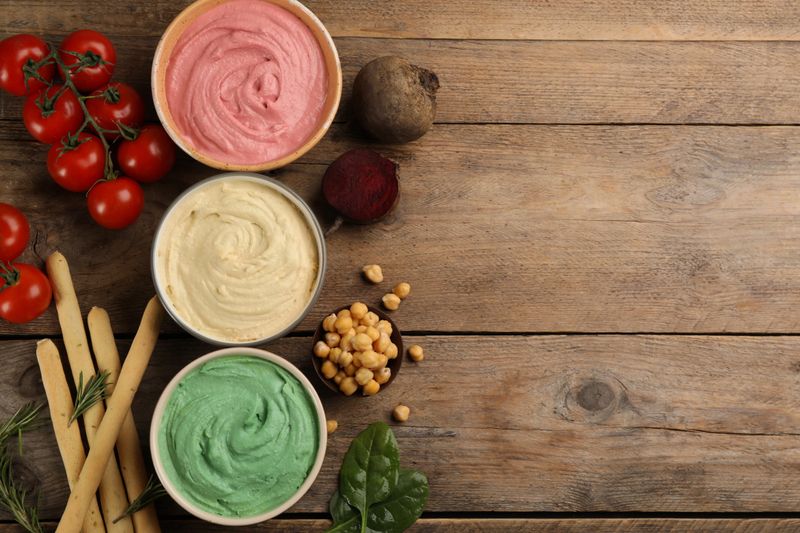 Different kinds of tasty hummus with bread sticks on wooden table, flat lay