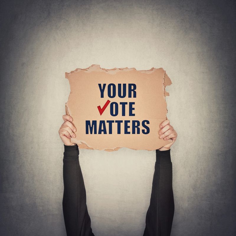 Activist hands holding up a cardboard banner with text message your vote matters, isolated on gray wall background. People legal and democratic rights, every voice counts. Election campaign agitation