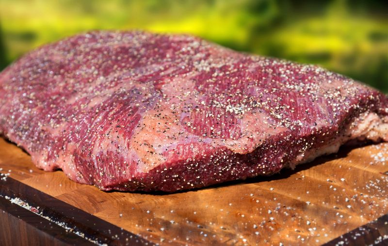 Large portion of seasoned tender lean raw beef brisket for roasting standing ready for cooking on a wooden chopping board in a close up low angle
