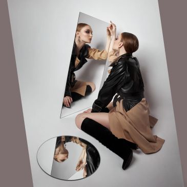Woman in a leather jacket interacting with her reflection in two mirrors.