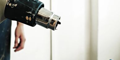 Close-up of a heat gun blowing hot air, with a blurred hand in the background.