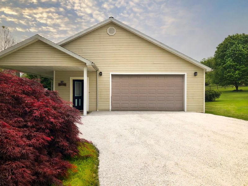 Freshly laid chip and sealed driveway leads to the attached garage of a ranch house. There is a Japanese Maple highlighting the image. There is copy space in the driveway itself