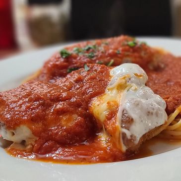 Cheesy meatballs covered in rich tomato sauce on a white plate.