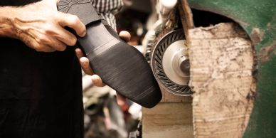 Schoenmaker werkt aan schoen onder een slijpmachine.