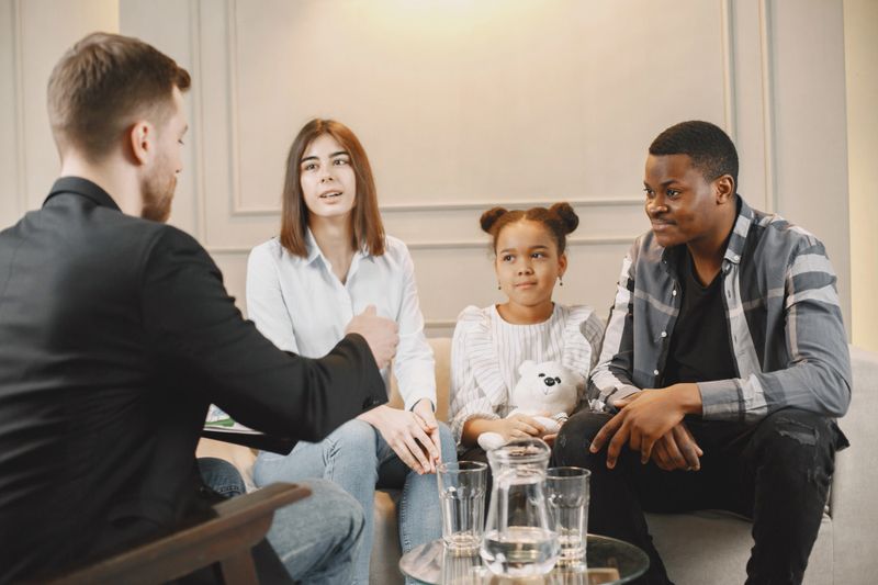Family counseling session at home with therapist. Pshycologist showing pictures of emotions to a girL.African American father and European mother.