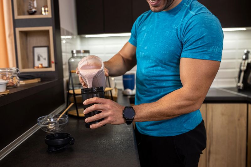Young man pouring a tasty berry shake into his drinking cup in the kitchen, delicious healthy treats concept
