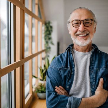 Smiling elderly man in glasses by window.