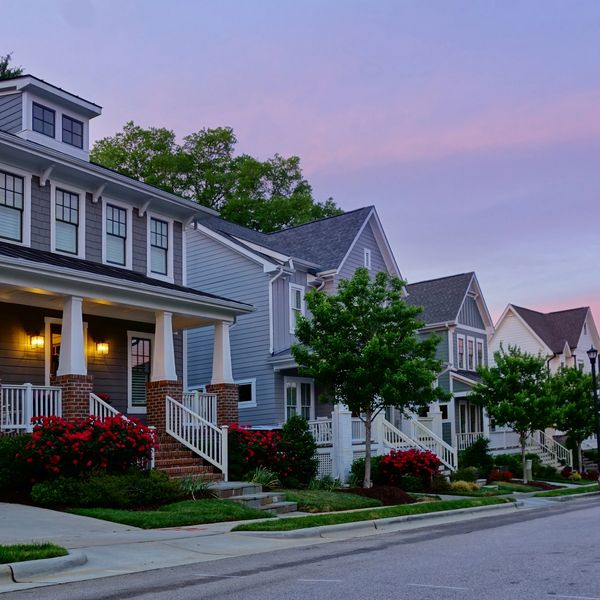 A row of suburban houses with porches and well-kept gardens at sunset.