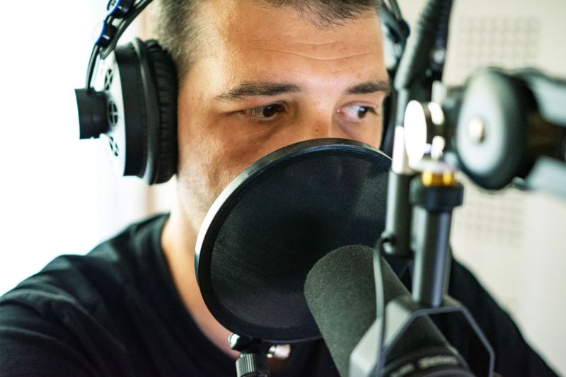 Portrait  of young male radio host going live on air talking in microphone in studio