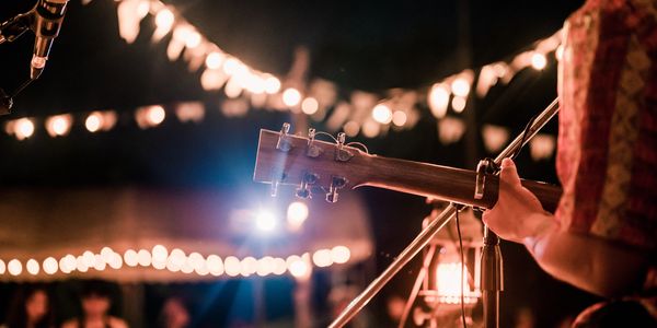 Musician playing guitar at a cozy outdoor nighttime event with string lights.