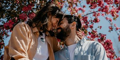 Couple sharing a tender moment under blooming pink trees.