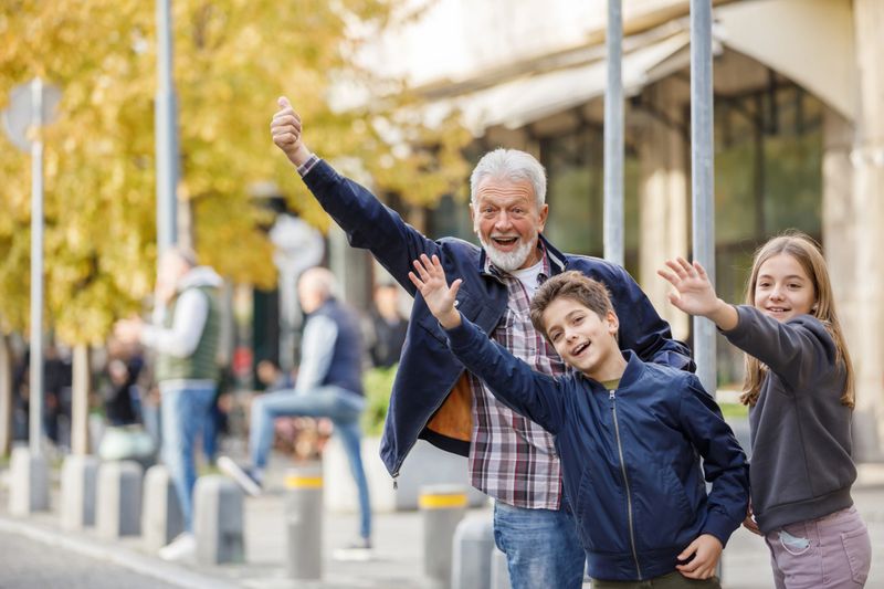 Portrait of Senior Man Walking in the Street With Grandchildren and Waving to Catch the Taxi. An Elderly Man and Cute Kids are in Rush and Looking for a Cab.