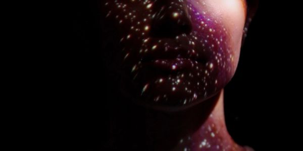 Woman's face illuminated with galaxy-like star projections in darkness.