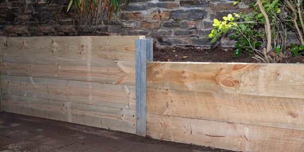 Wooden raised garden beds with soil and plants against a stone wall.