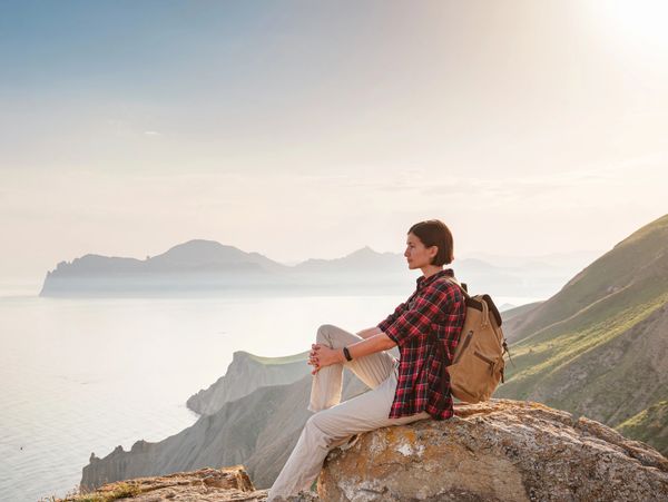 Woman resting on a rock overlooking a misty coastal mountain landscape at sunrise.