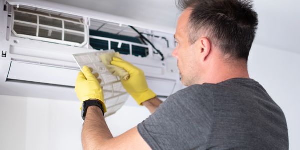 Man wearing yellow gloves cleaning an air conditioner filter.