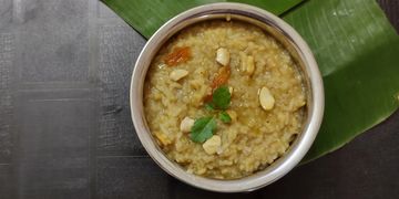 A bowl of Indian sweet pongal garnished with cashews and raisins on banana leaf.