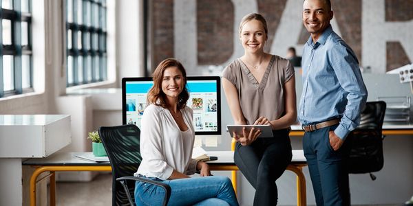 Three professionals smiling in a modern office workspace.