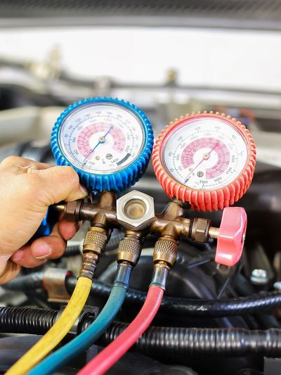 Hand holding HVAC manifold gauges on a car engine for air conditioning service.