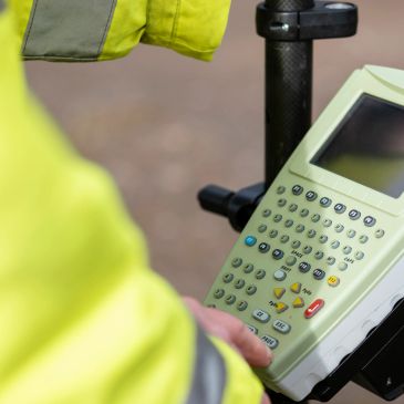 Person operating a surveying device wearing a high-visibility jacket.