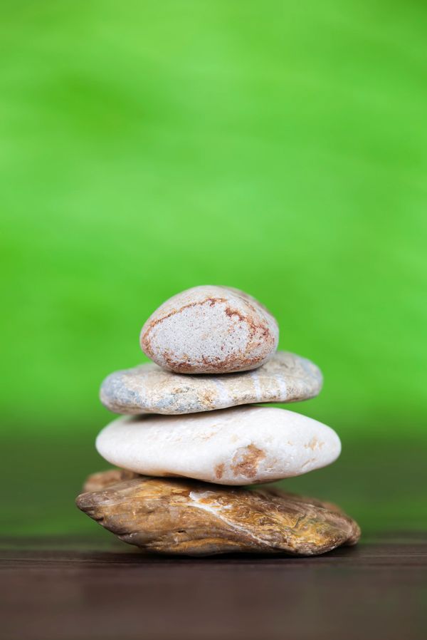 Stack of smooth stones balanced on a wooden surface with a green blurred background.