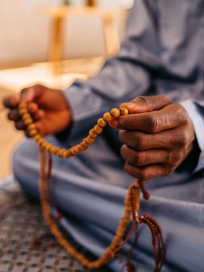 Person holding prayer beads while sitting cross-legged indoors.