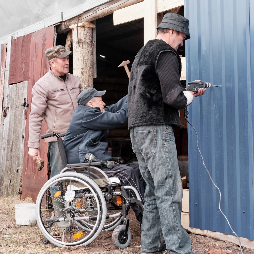 Three men, one in a wheelchair, working together to fix a door with tools.