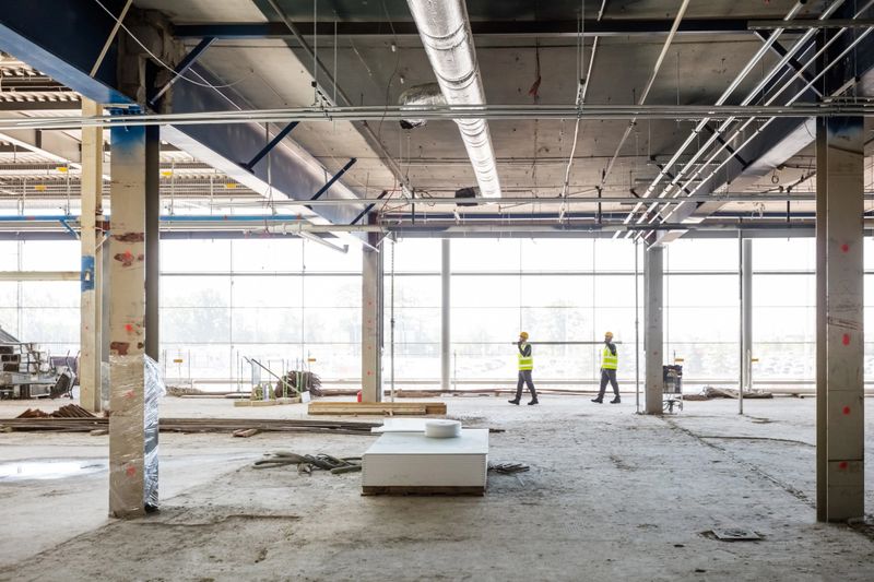 Two workers wearing work helmets and reflective vests holding long pipe at the construction site. Wide angle view.