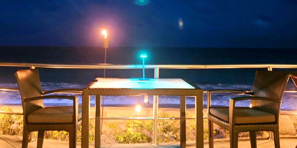 Two chairs and a table with ocean view at night, illuminated by soft lights.