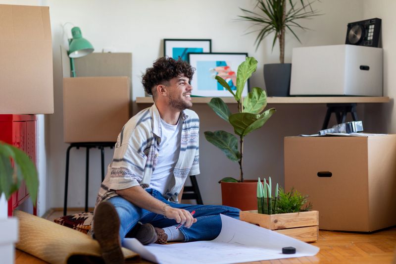 Young Caucasian man moving into his new home and starting a new life, looking at a home improvement plan and deciding how to start implementing it, smiling