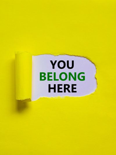 Text 'YOU BELONG HERE' revealed under torn yellow paper.