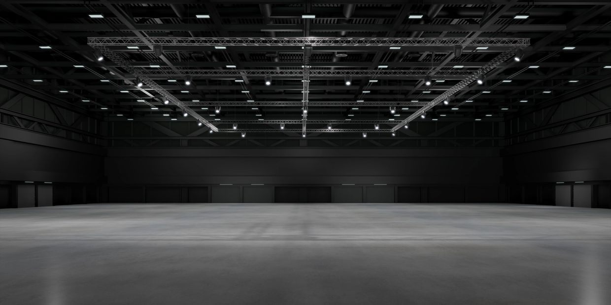 Empty industrial warehouse with overhead lighting and concrete floor.