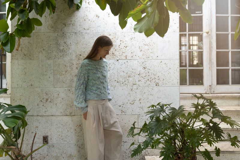 Moody images of blonde, Scandinavian woman in her forties wearing home knitted sweater. The images portrait a female relaxing in her winter garden while being thoughtful and enjoying the surroundings of plants, trees and sunshine