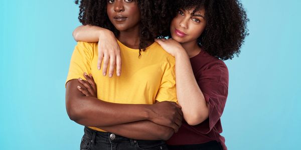 Two women with curly hair embracing against blue background.