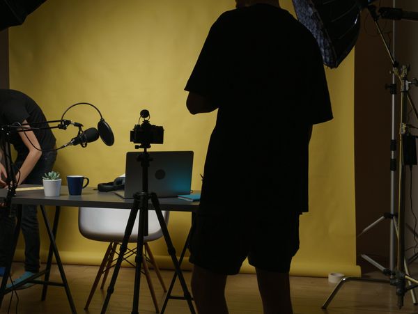 People setting up video recording equipment in a studio with yellow backdrop.